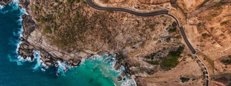 Aerial view of road going through beautiful landscape. Rocky scenery close to the ocean.
