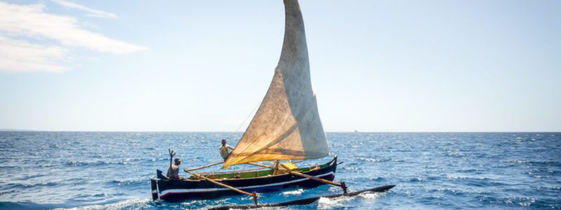 View of Nosy Komba Island coastline with a sail boat sailing on the sea, Nosy Komba, Madagascar