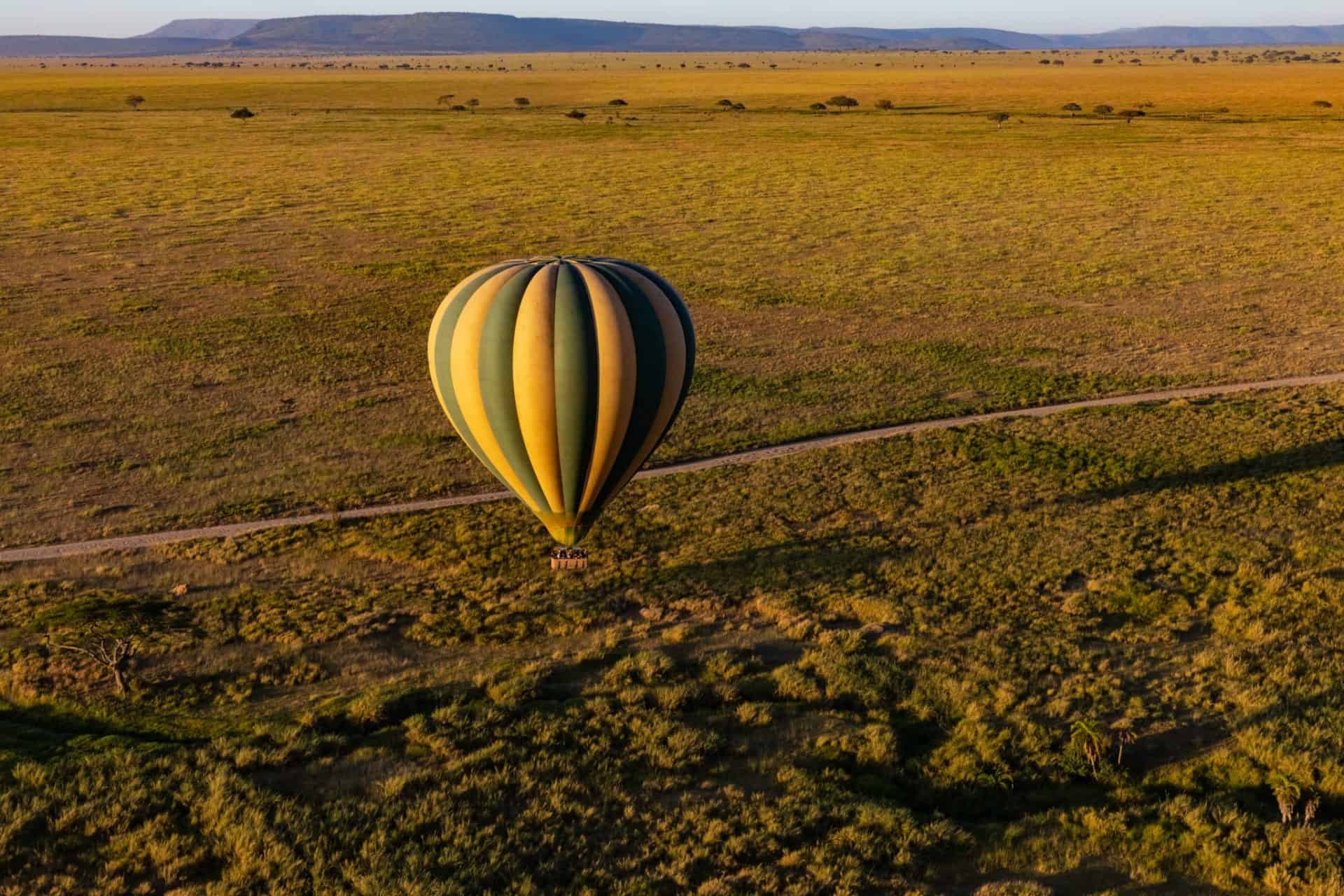 Green and yellow hot air balloon flying over the Serengeti National Park, in Tanzania.