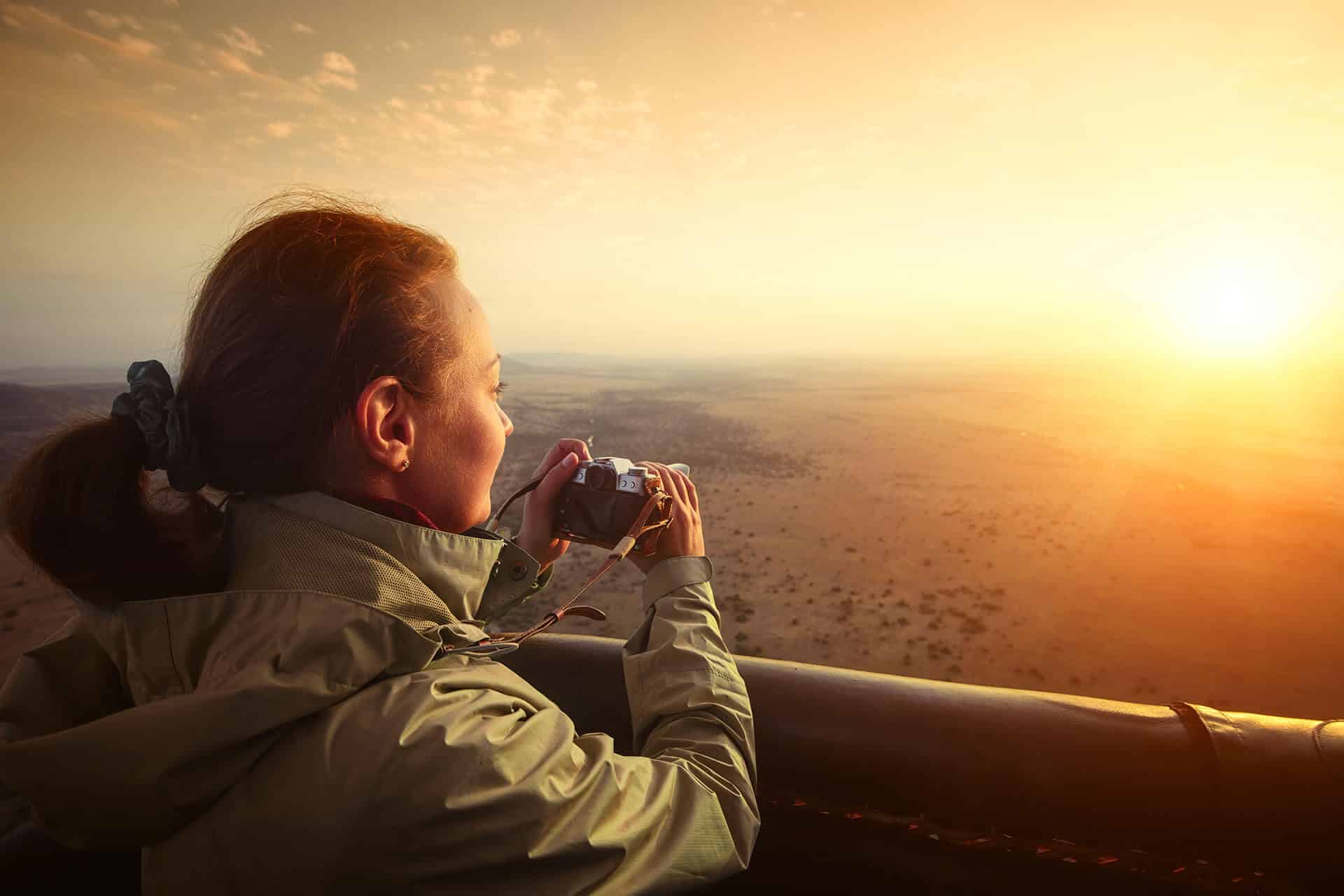 Lady taking a picture from a hot air balloon in the early morning