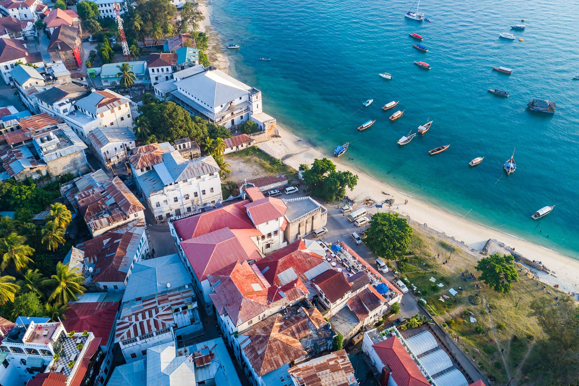 Zanzibar Stone Town aerial overview of red and white roofed buildings and clear blue ocean with white sand.