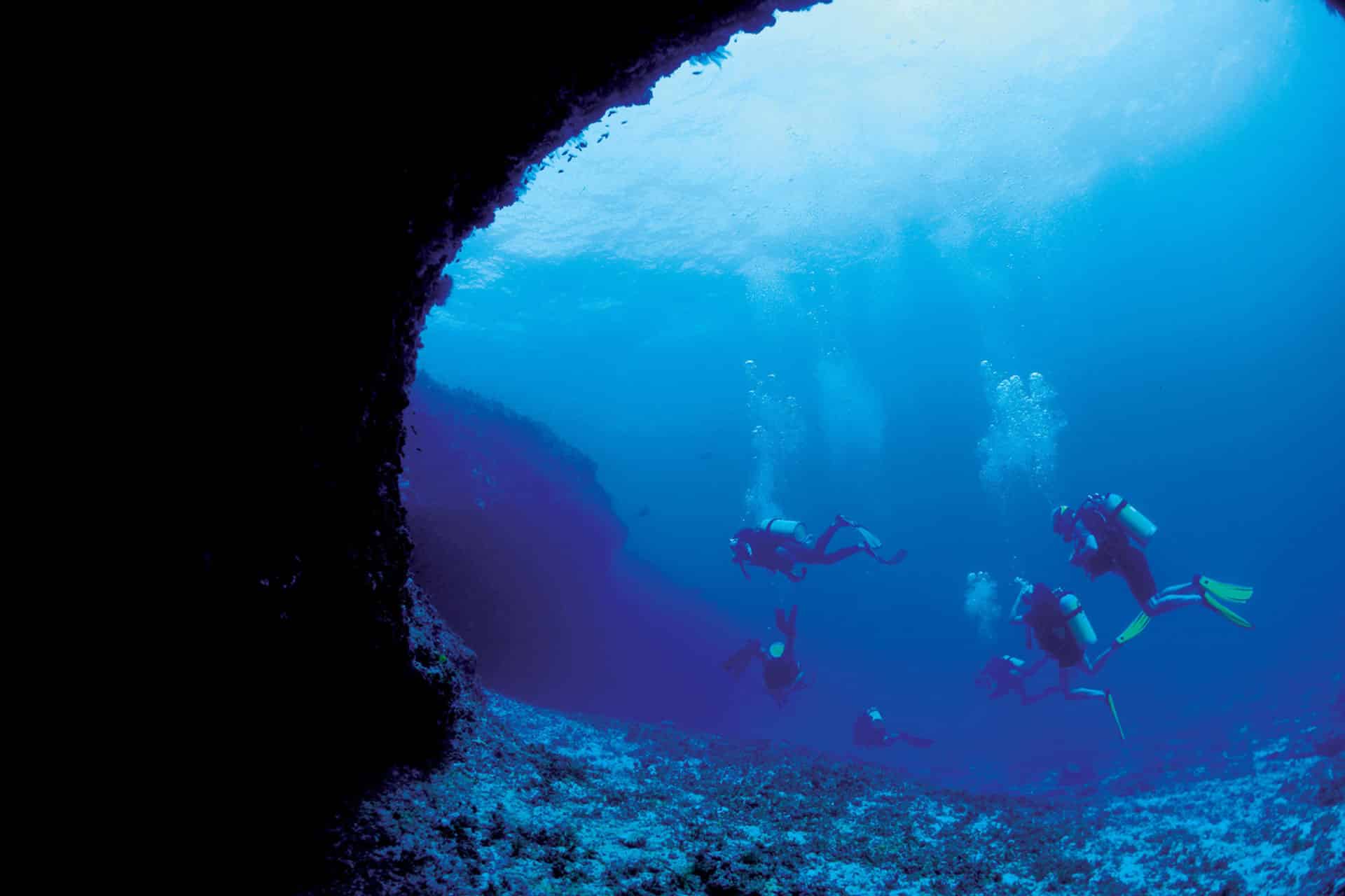 Scuba divers swim past a cave near Four Seasons Desroches, Seychelles.