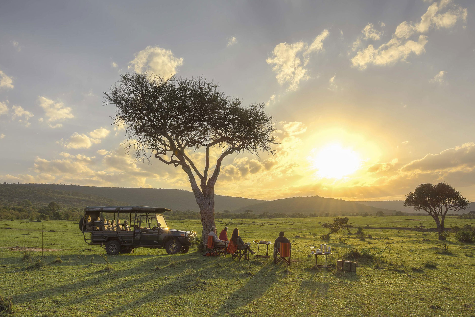 People sitting next to a car watching the sunset in the African bush