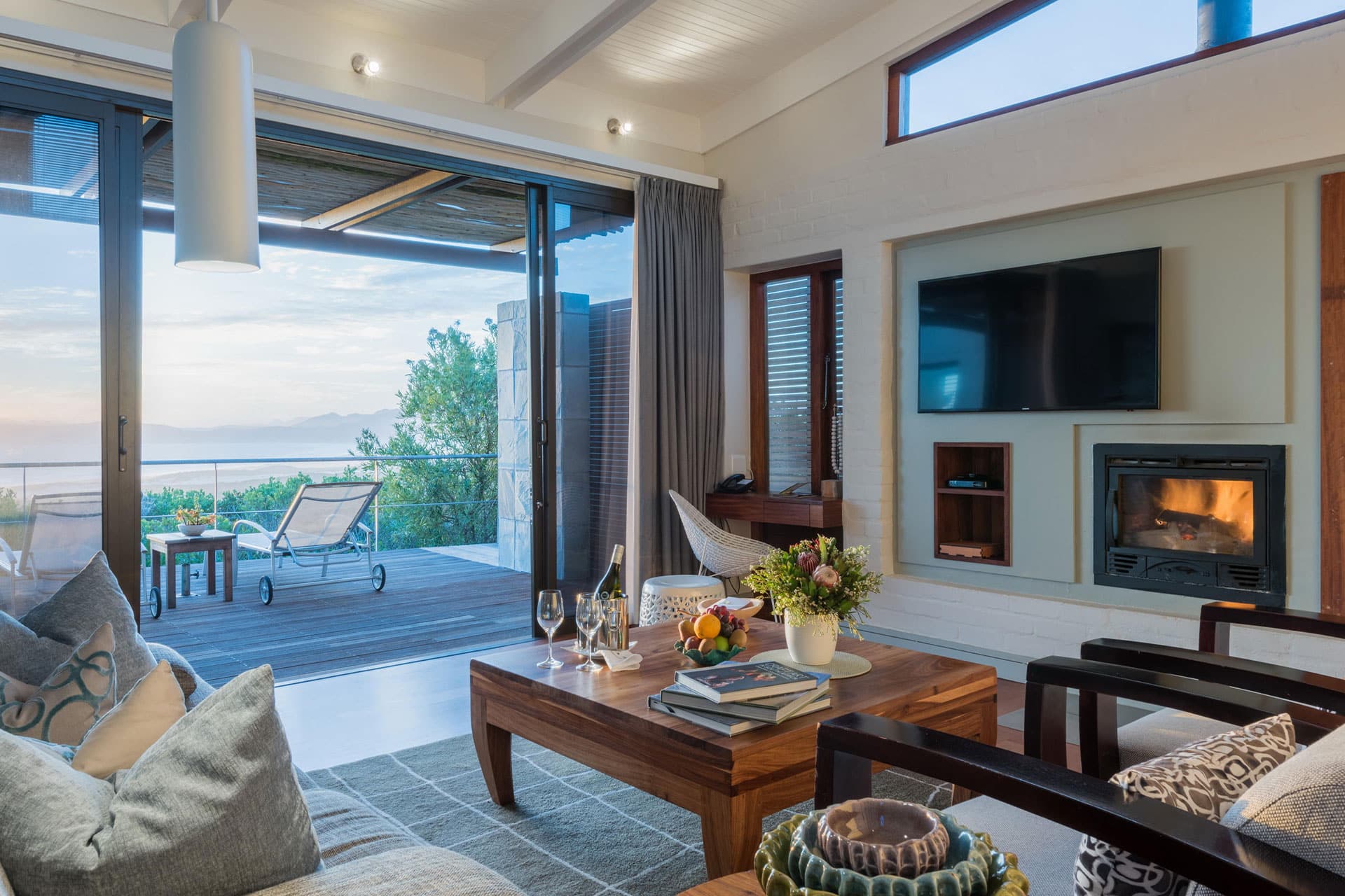 A hotel suite lounge with TV and fireplace and a view at Grootbos Private Nature Reserve