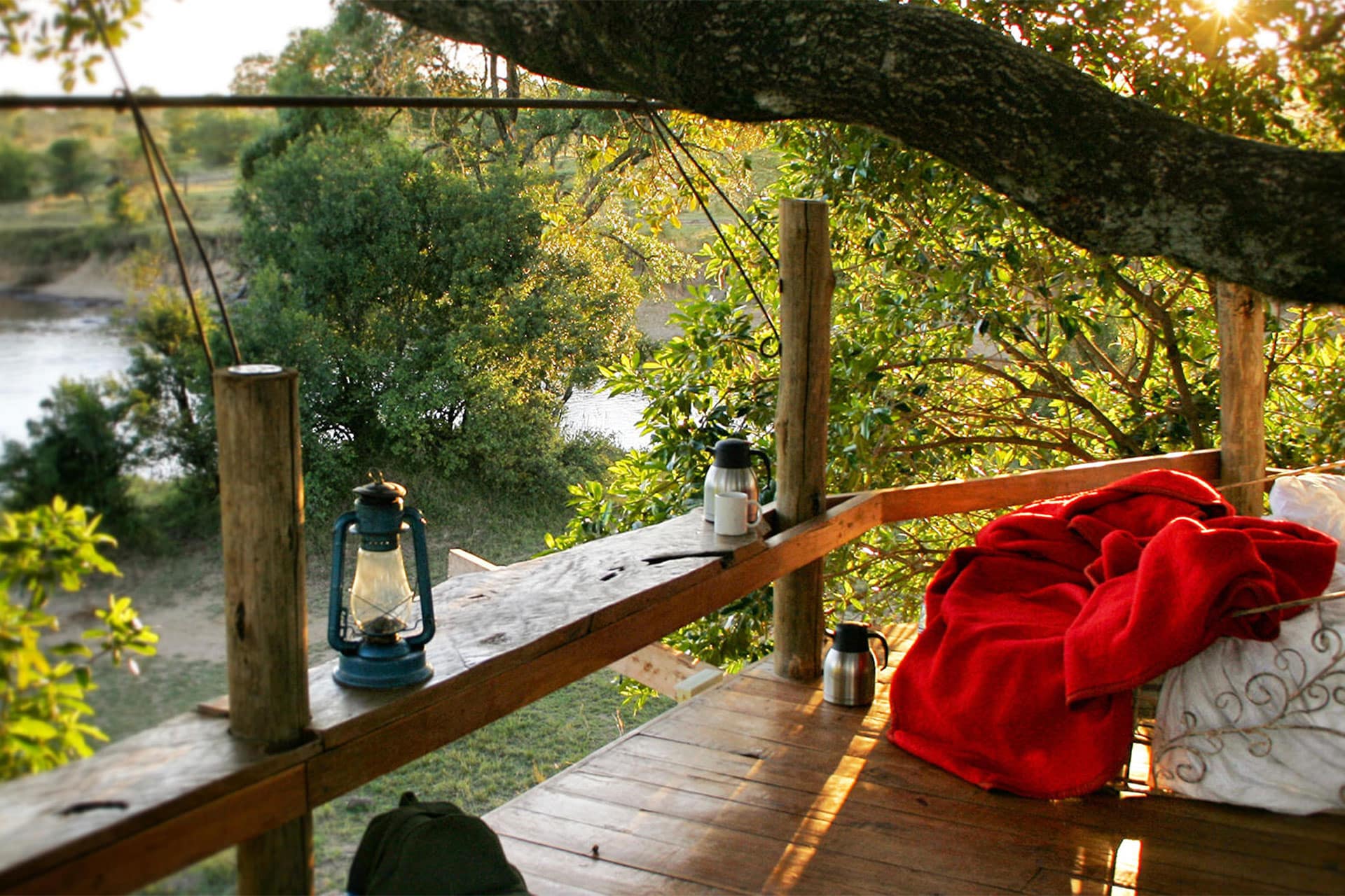 A gas lamp and bed in a treehouse overlooking a river during a night safari.