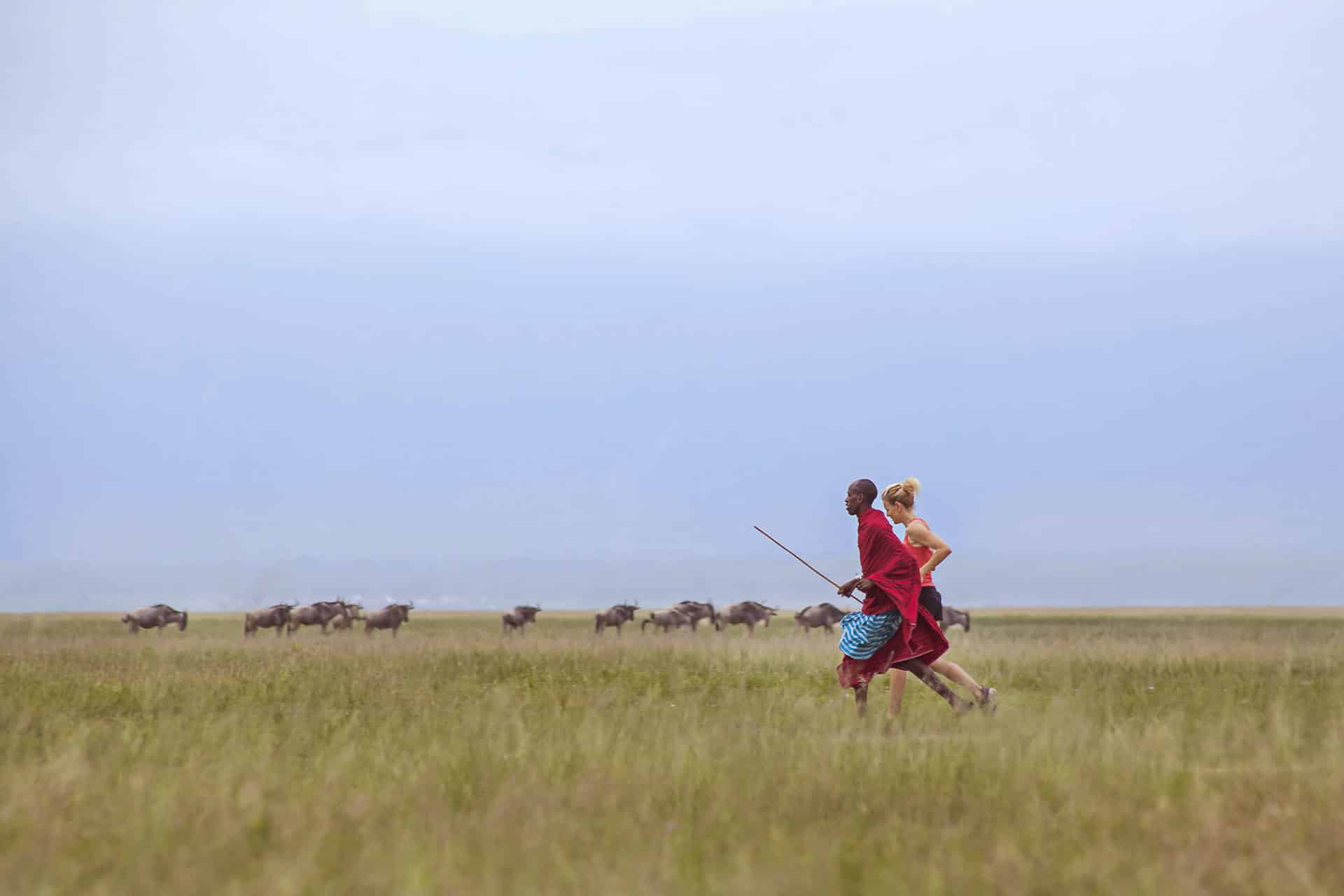 A woman and a Maasai warrior running in the bush.