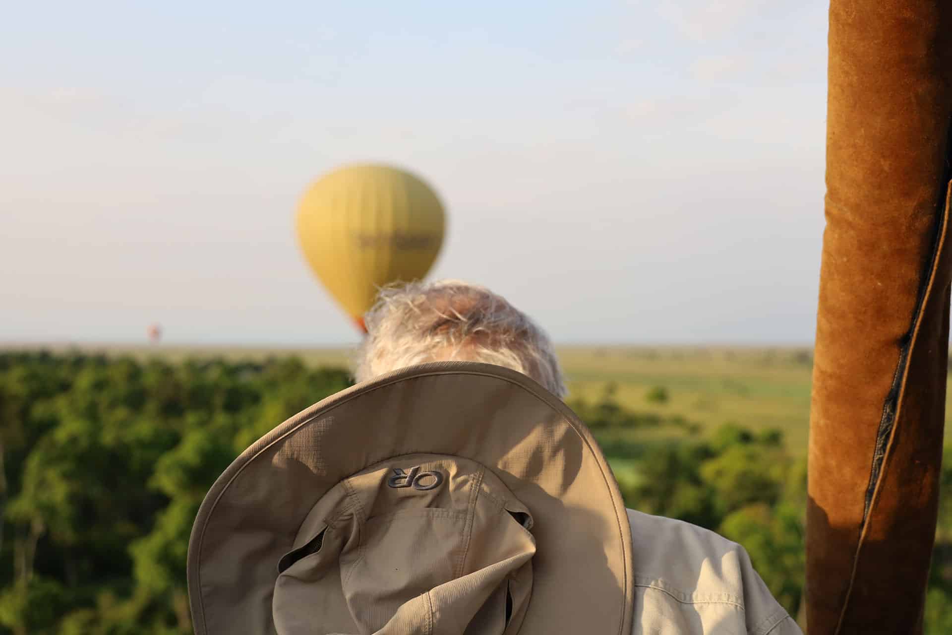 A man with a hat covering his face and a hot air balloon in the Maasai Mara in Kenya.