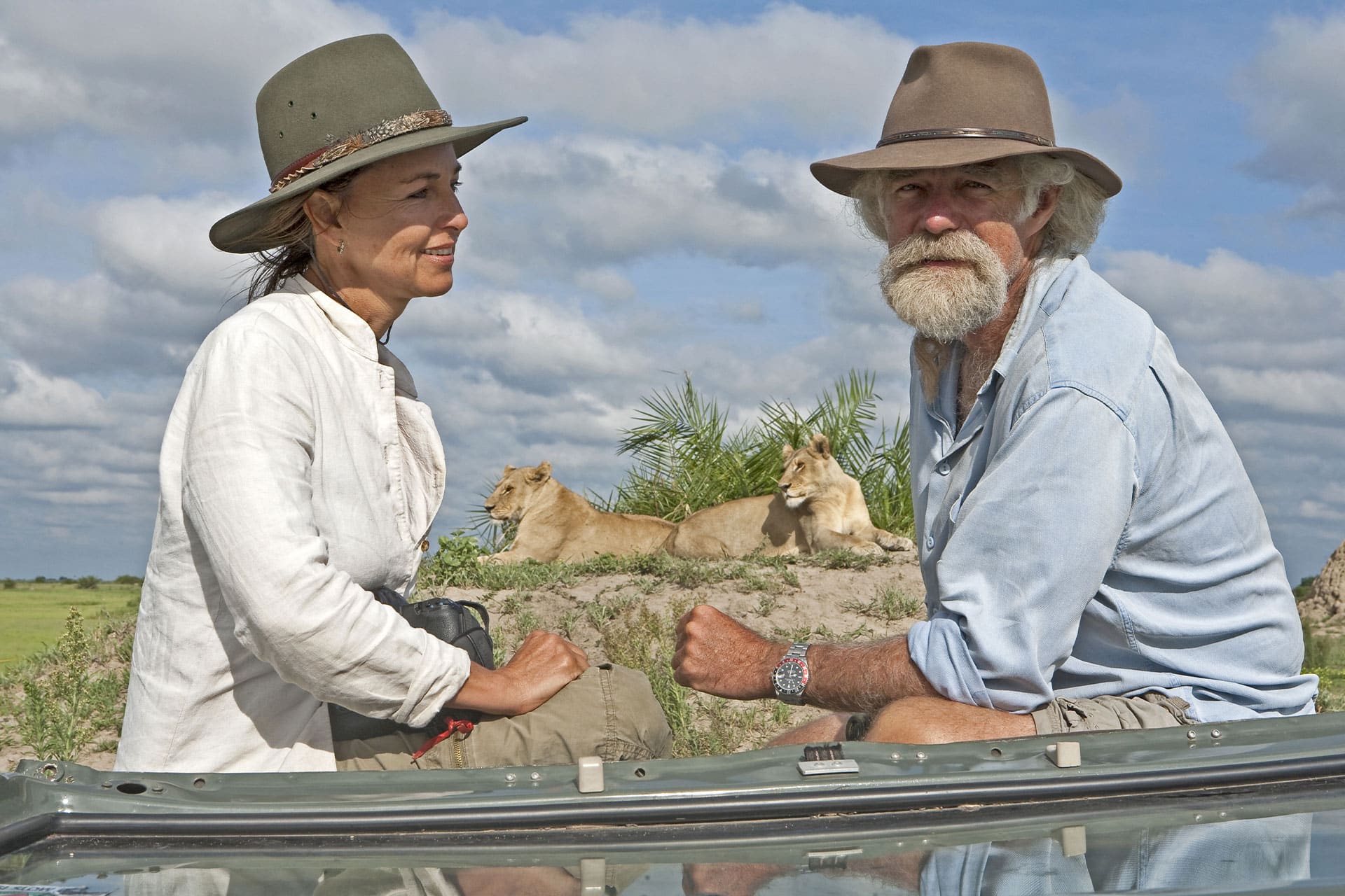 Dereck and Beverly Joubert posing with two female lions in the background.
