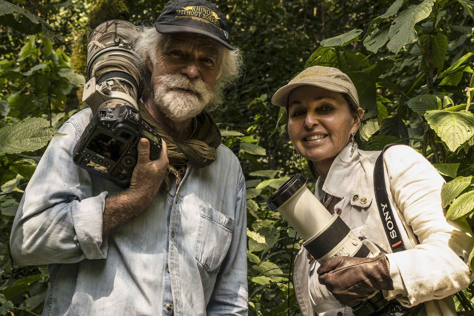 Photographers and filmmakers, Dereck and Beverly Joubert standing holding their cameras in the wilderness in Botswana.