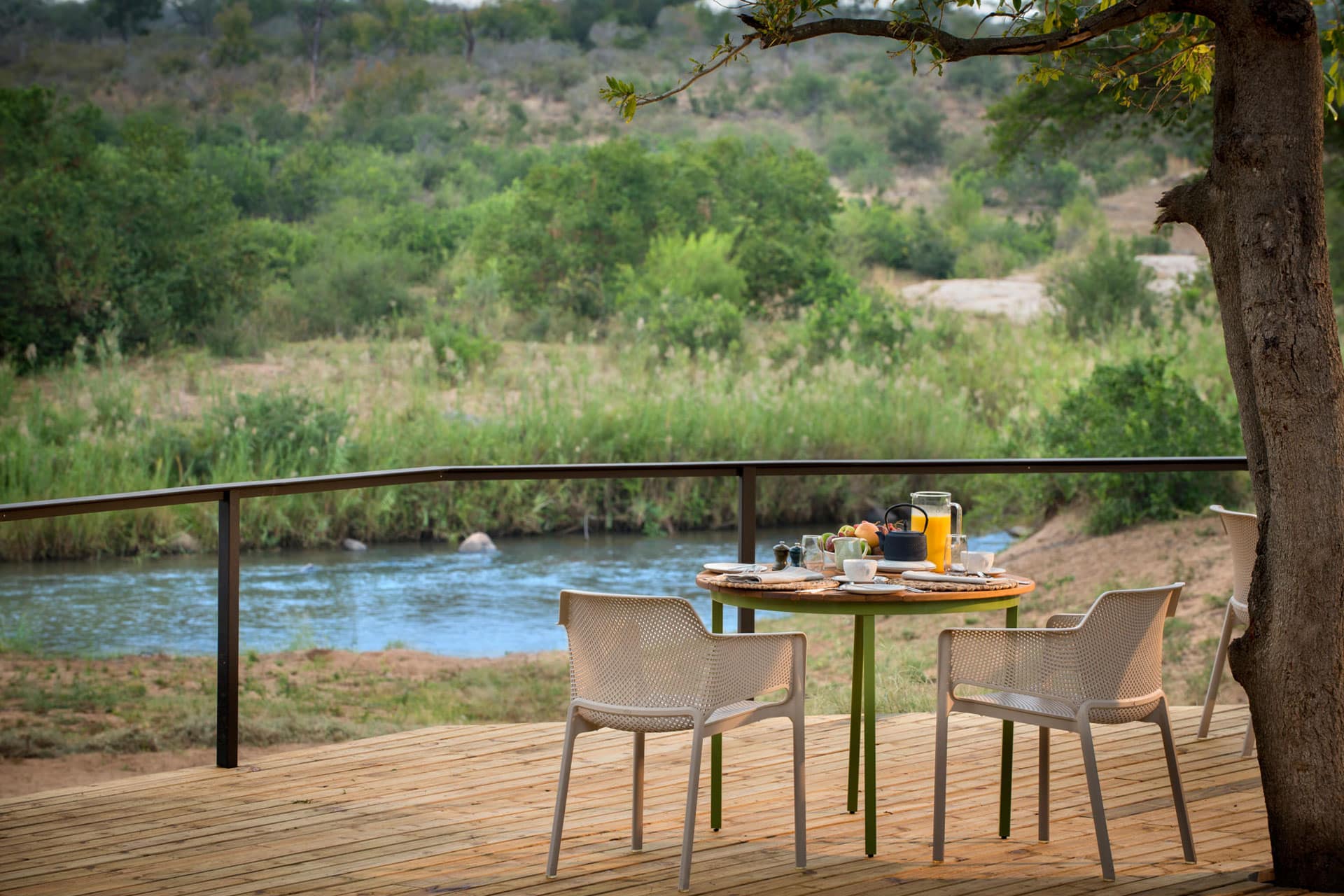A breakfast table set up on a wooden deck overlooking the river at Lion Sands River Lodge in Lion Sands Game Reserve.