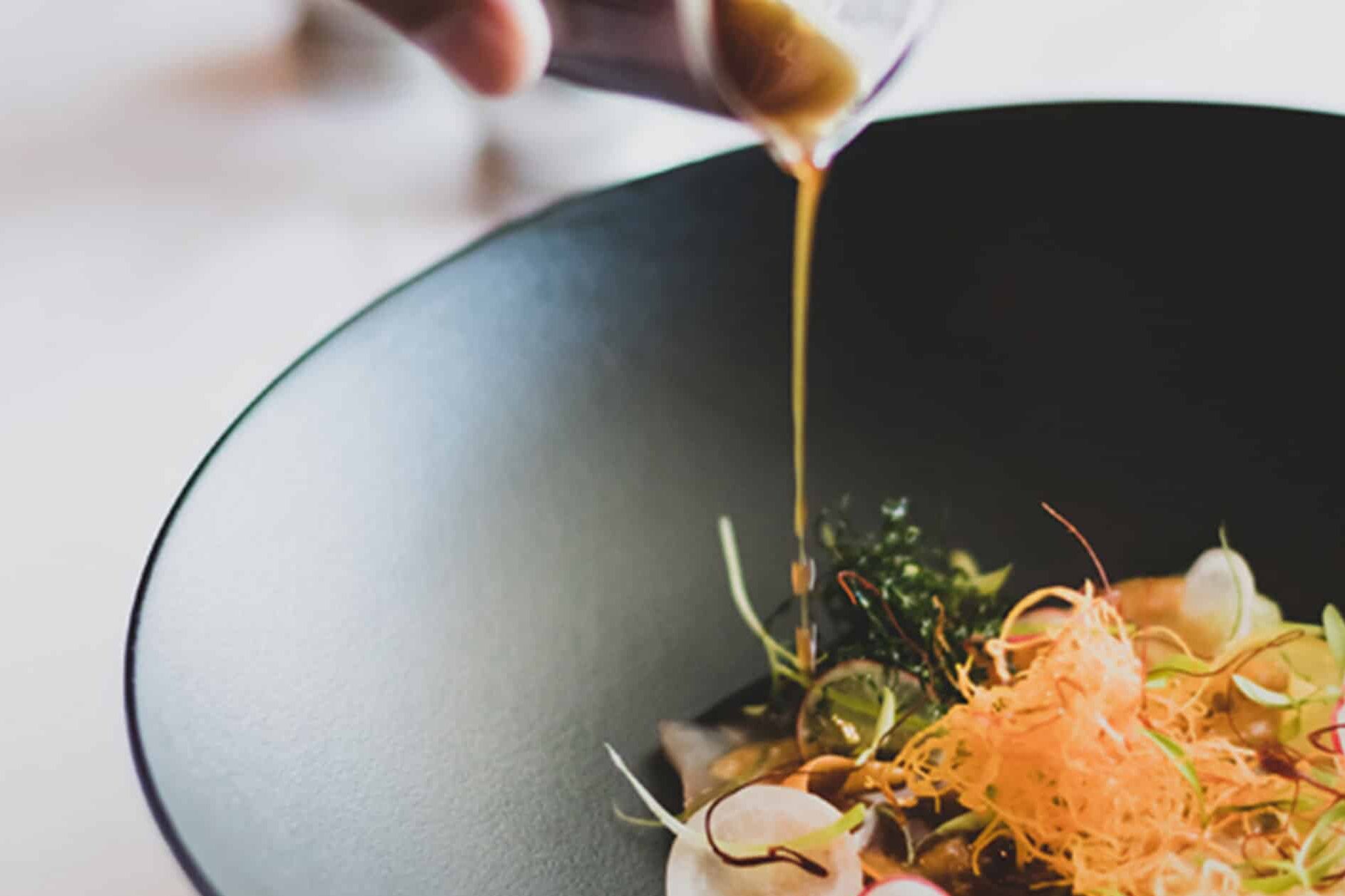 A chef pouring liquid onto a plated dish at Salsify at the Roundhouse – one of the top 10 fine dining restaurants in Cape Town. 