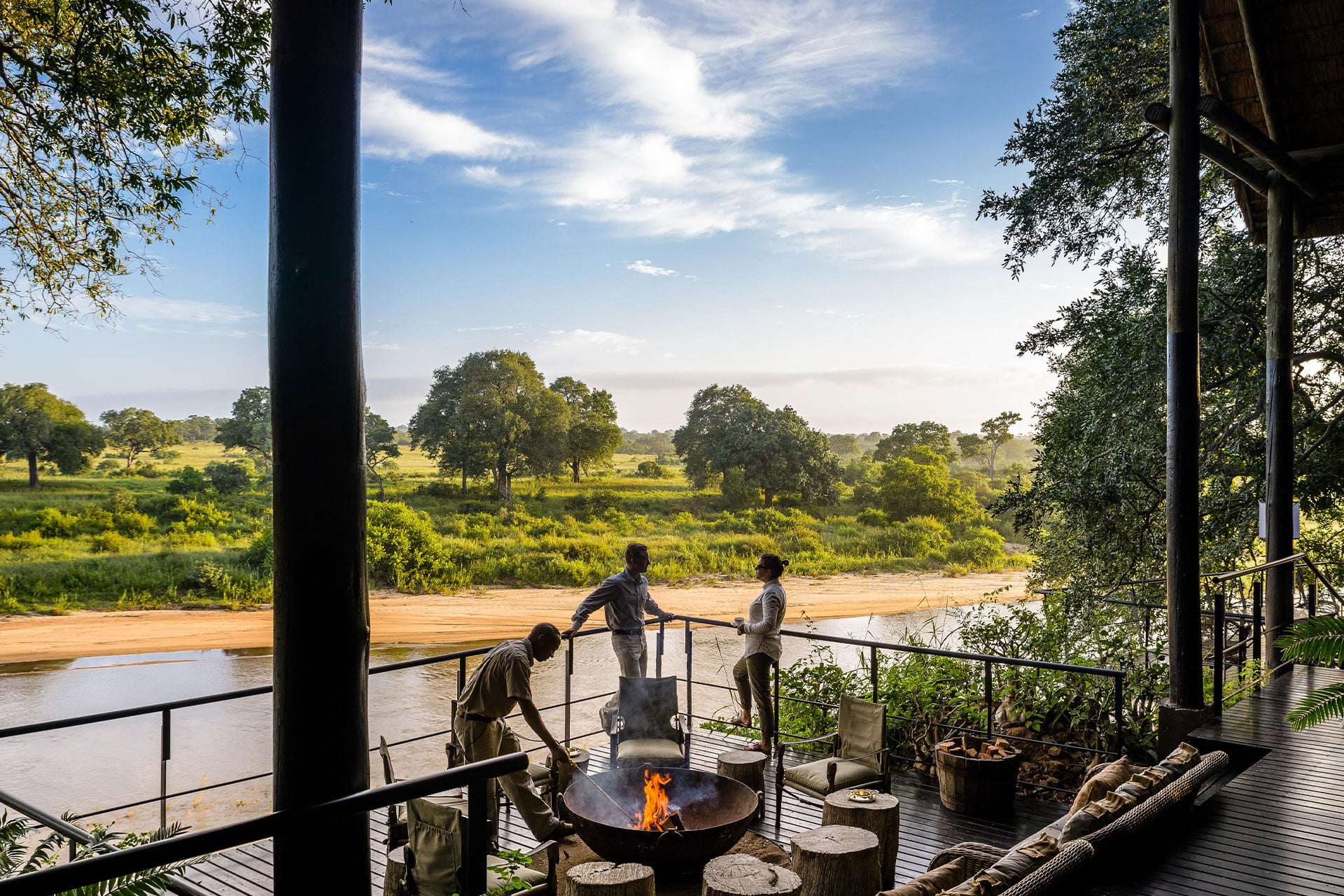 People gathered around the fire pit on the wooden deck with views of the Sand River at Singita Sabi Sands Ebony Lodge.