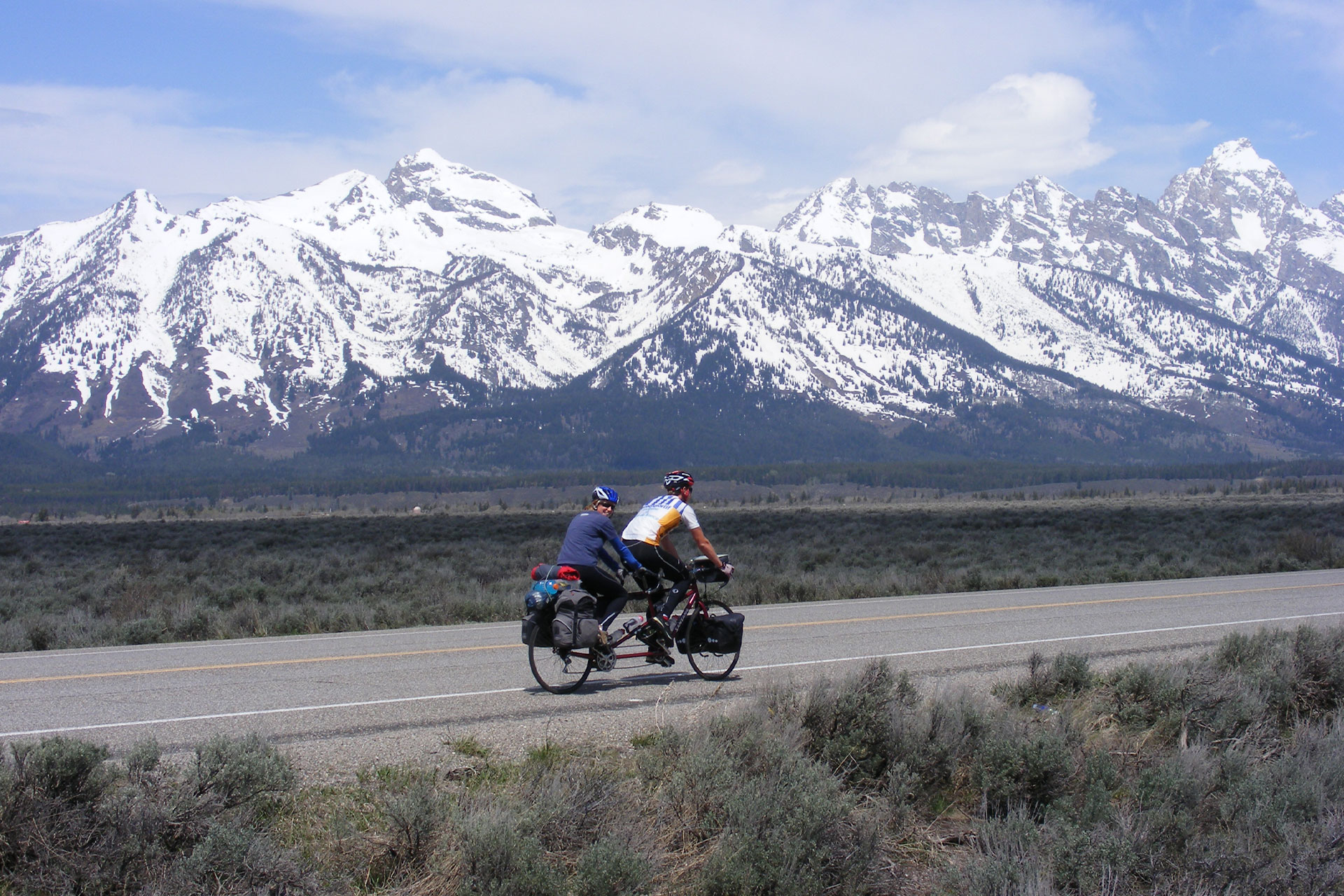 Holly Tuppen and her partner on a tandem bike with snow capped mountains in the background.