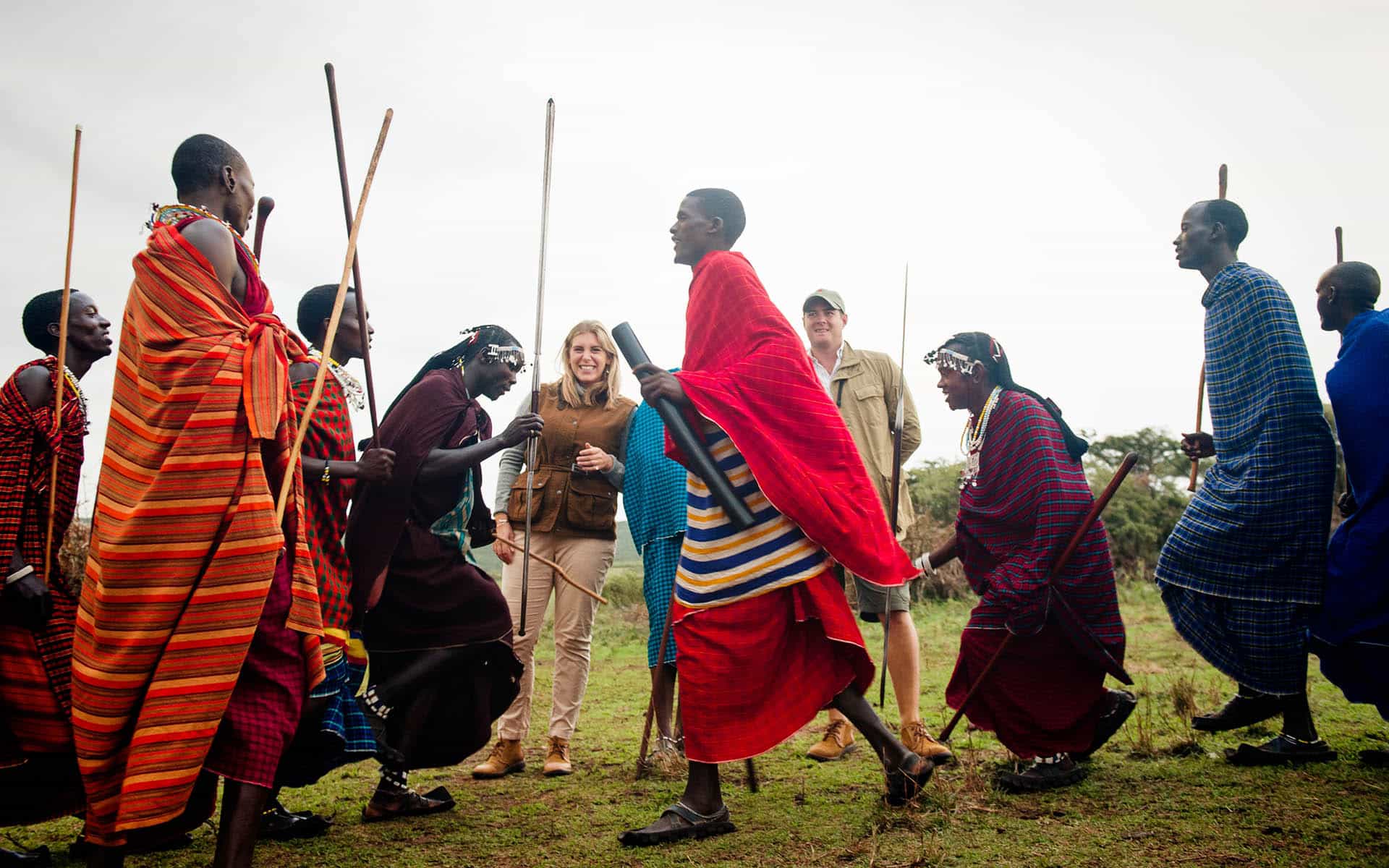 Group of Maasai people dancing with two travelers.