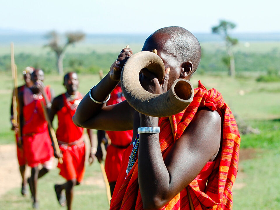 Maasai man blowing a kudu horn on safari with Ker & Downey® Africa