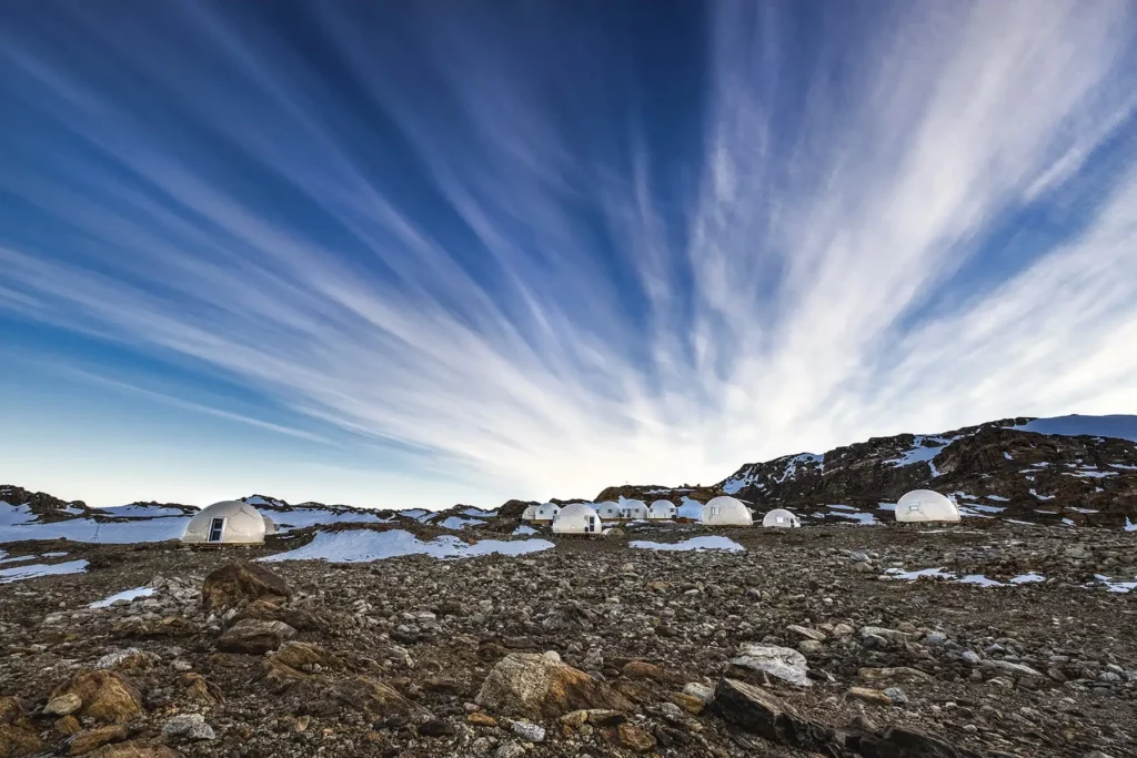 Luxury expedition camp set on a remote polar landscape during a cape town to antarctica journey, featuring modern dome tents surrounded by rocky terrain and patches of snow under dramatic skies