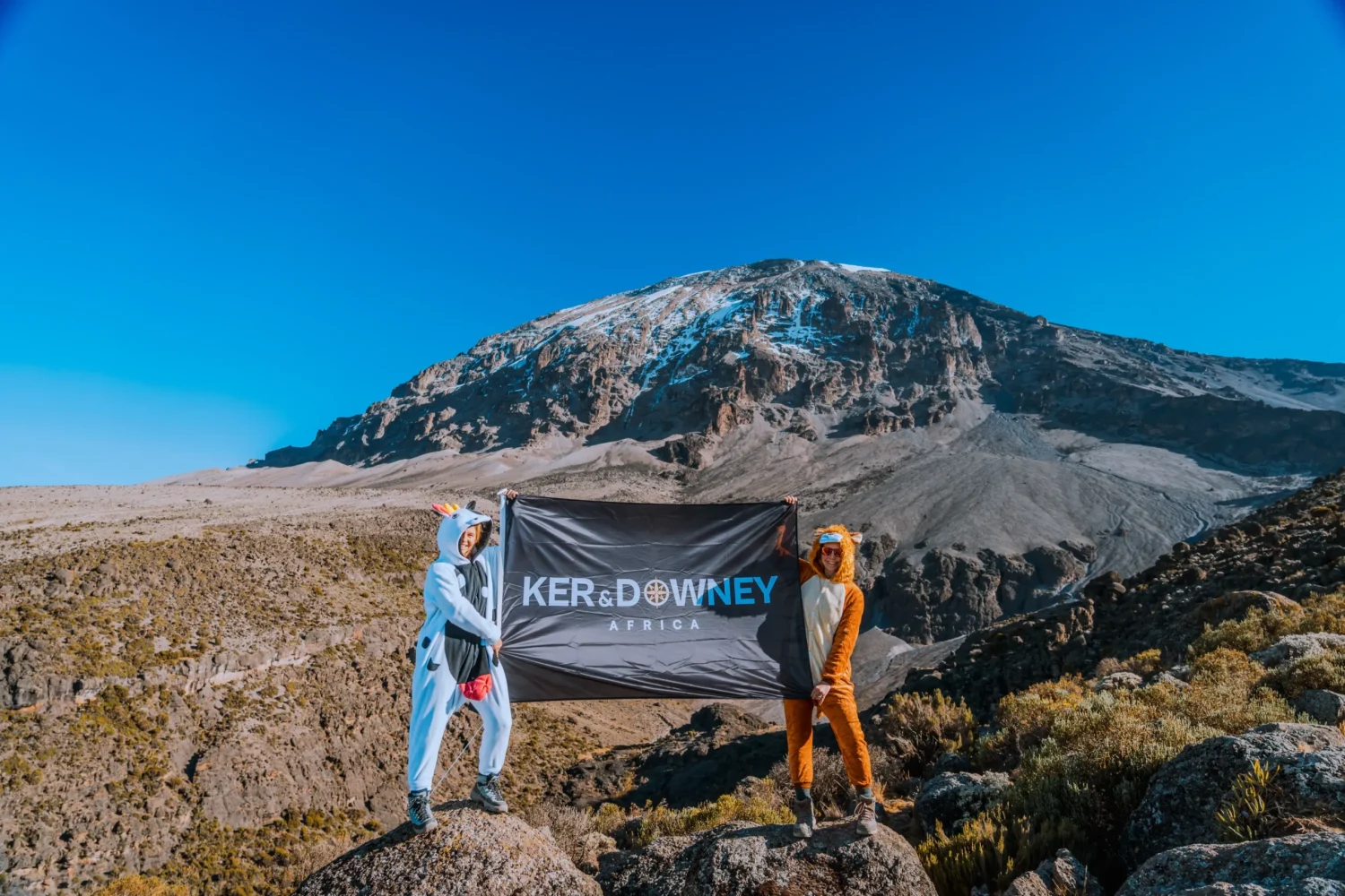 The team from Ker & Downey Africa holding the flag in front of Mount Kilimanjaro