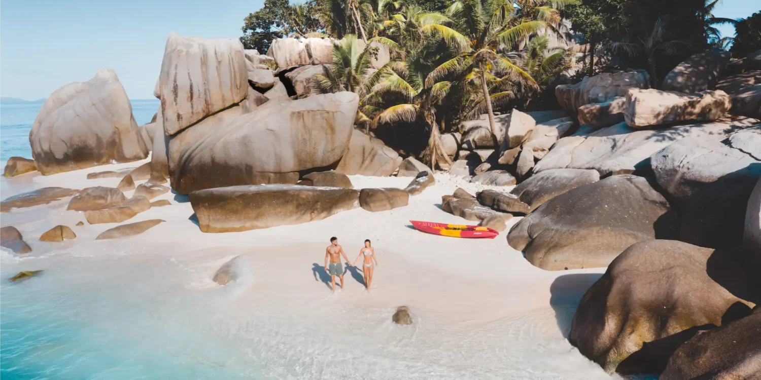 Couple walking along a secluded white sand beach with granite boulders and turquoise water during Africa’s Secret Season, highlighting a private island experience