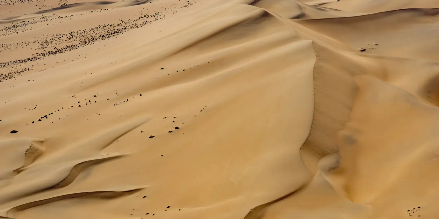 Sweeping aerial view of golden desert dunes shaped by wind in Africa’s Secret Season, revealing untouched wilderness and dramatic natural patterns