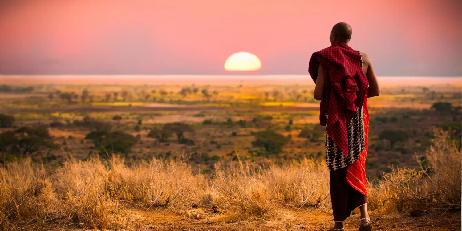 Maasai warrior overlooking the savannah at sunset in Africa’s Secret Season, with golden light stretching across the open plains of East Africa