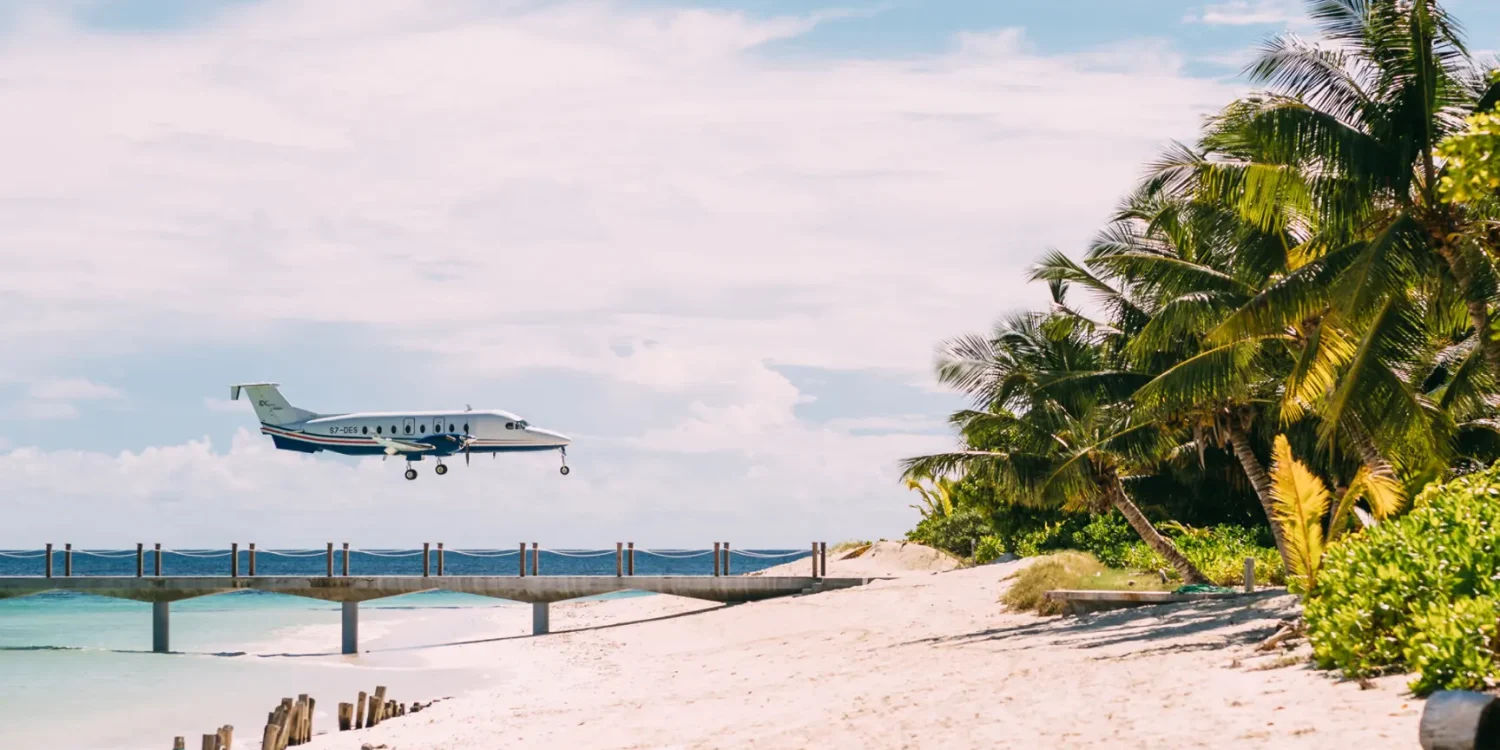 Luxury safaris by air Africa private light aircraft landing on a tropical island runway beside palm trees and turquoise ocean