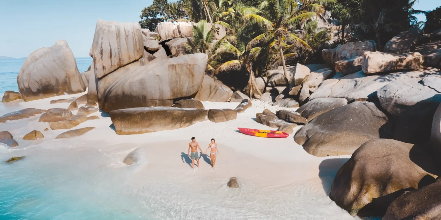 Couple walking on a secluded tropical beach with granite boulders during Luxury safaris by sea Africa journey