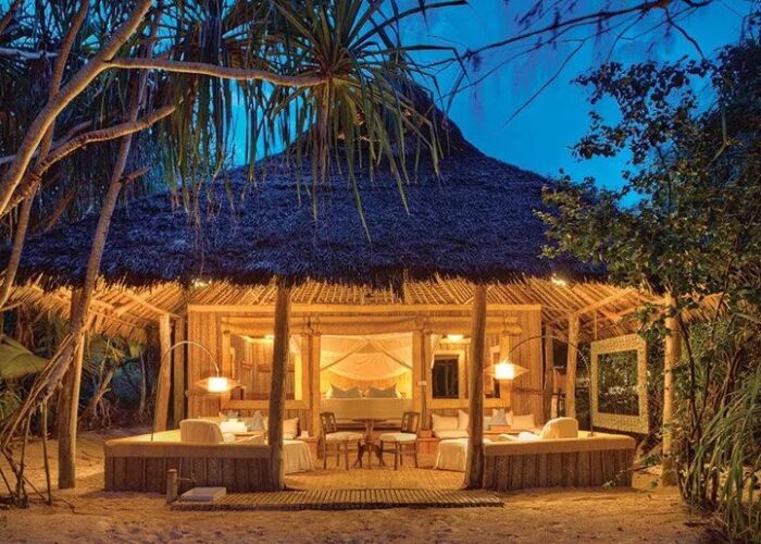 Thatched luxury beach villa glowing at dusk among tropical greenery on serene Islands in Africa