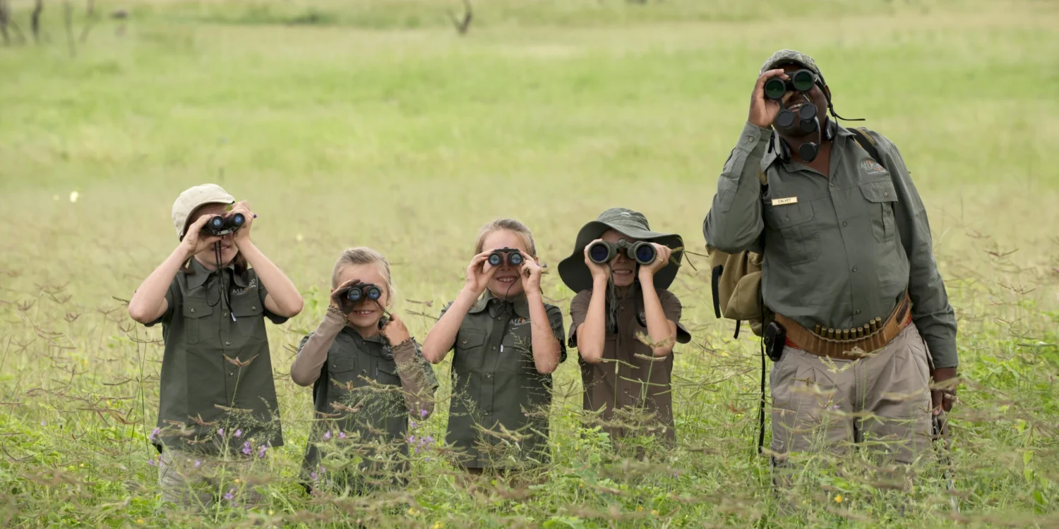 children on safari with a local guide using binoculars for wildlife observation during a winter holiday safari school.