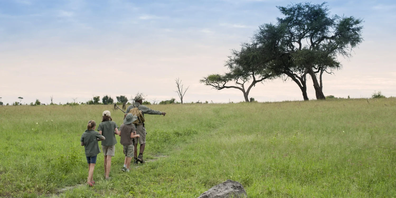 children walking with a safari guide across a green savannah landscape under a pastel sky during a long weekend safari adventure.