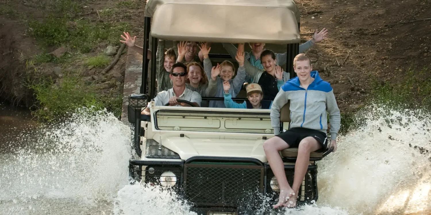 Teenagers enjoying a thrilling river crossing in safari vehicle on an African safari for teenagers